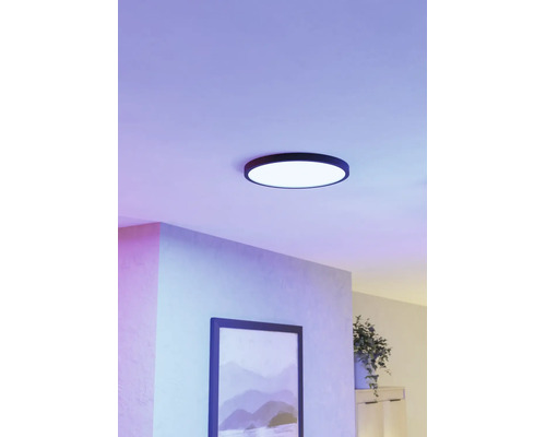 Ronde LED plafondlamp met een zwart frame in een modern ingerichte kamer met paars licht en een schilderij aan de wand.