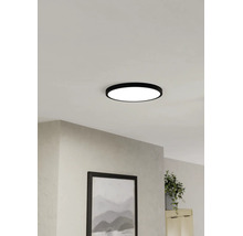 Platte, ronde LED-plafondlamp met zwarte rand, gemonteerd aan het plafond in een lichte woonkamer.