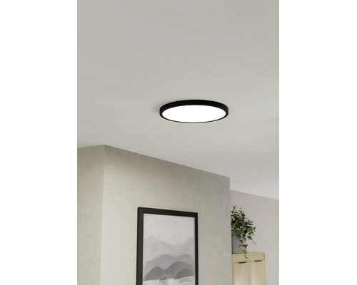 Platte, ronde LED-plafondlamp met zwarte rand, gemonteerd aan het plafond in een lichte woonkamer.
