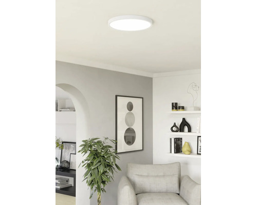 Platte ronde LED-plafondlamp in een modern ingerichte woonkamer met een fauteuil, kamerplant en wanddecoratie.
