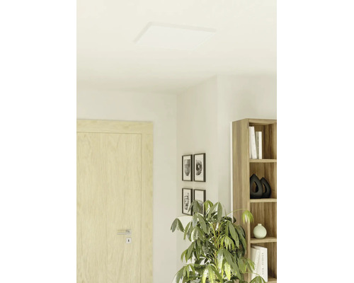Vlak, vierkant LED-paneel als plafondlamp in een lichte, moderne woonkamer met houten deur en kamerplant.