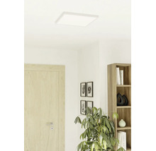 Vlak, vierkant ledpaneel aan het plafond in een lichte, modern ingerichte kamer met een houten deur, boekenkast en kamerplant.