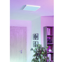 Modern vierkant LED-paneel aan het plafond van een woonkamer met violette verlichting, houten deur, boekenplank en kamerplant.
