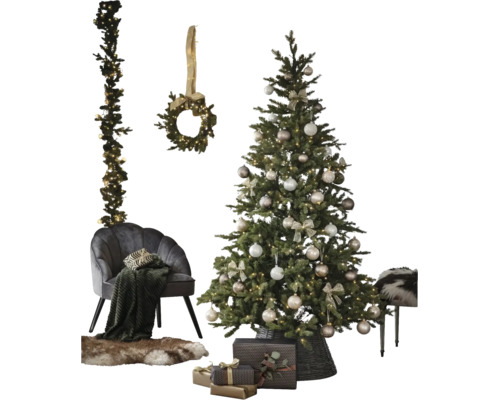 Versierde kunstkerstboom met kerstballen en verlichting naast een fauteuil, krans, slinger en cadeaus.
