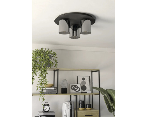 Drieliichts plafondlamp met cilindrische glazen kappen in een lichte, modern ingerichte kamer boven een plank met boeken en planten.