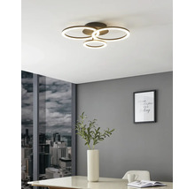 Moderne LED-plafondlamp met vier lichtgevende ringen in een lichte kamer met grijze muur, uitzicht op de stad en een witte tafel.