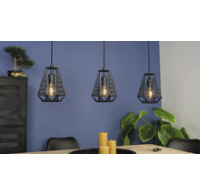 Drie zwarte hanglampen in kooiontwerp boven een houten tafel in een modern ingerichte kamer met planten.