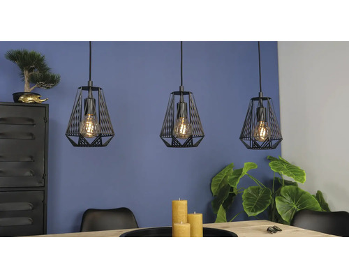 Drie zwarte hanglampen in kooiontwerp boven een houten tafel in een modern ingerichte kamer met planten.
