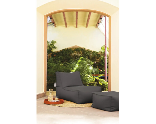 Antracietkleurige outdoor zitzak fauteuil met bijbehorende hocker op een jute tapijt in een tuinsetting.