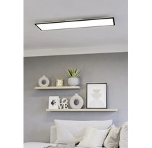 Rechthoekig LED-paneel met zwart frame aan het plafond boven een lichte, modern ingerichte woonruimte met planken en een bank.