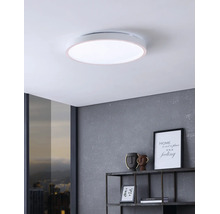 Platte, ronde LED-plafondlamp in een moderne kamer met een grijze wand en wandrek.