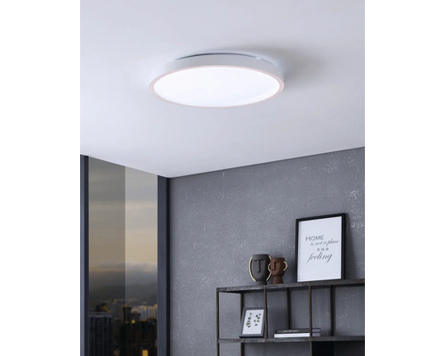Platte, ronde LED-plafondlamp in een moderne kamer met een grijze wand en wandrek.