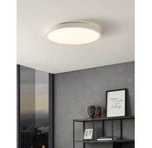 Platte, ronde LED-plafondlamp in een modern interieur met een gestructureerde wand en een metalen wandrek.