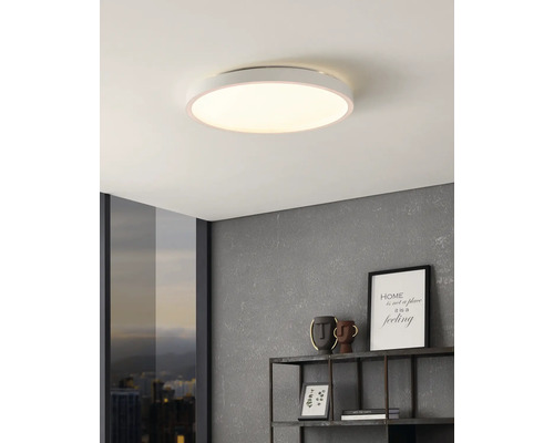 Platte, ronde LED-plafondlamp in een modern interieur met een gestructureerde wand en een metalen wandrek.
