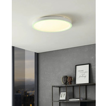 Platte ronde LED-plafondlamp in een moderne woonkamer met grijze muur met textuur, wandplank en raam met uitzicht op de stad.