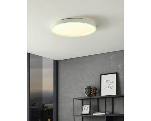 Platte ronde LED-plafondlamp in een moderne woonkamer met grijze muur met textuur, wandplank en raam met uitzicht op de stad.