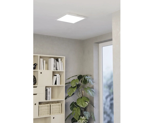 Vierkant LED-paneel aan het plafond in een modern ingerichte lichte kamer met boekenkast en grote kamerplant.