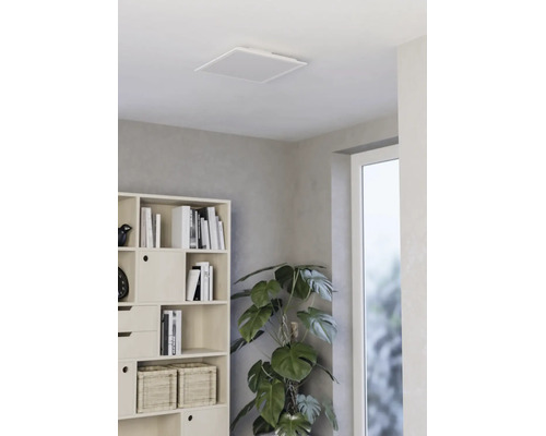 Vierkant LED-plafondpaneel in een lichte, moderne woonkamer met een stellingkast en een kamerplant.
