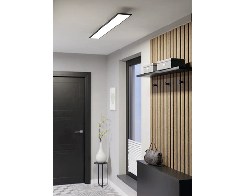 Moderne, lichte hal met een lange rechthoekige led-plafondlamp, een houten wandpaneel met haken, een zwarte deur en een raam.