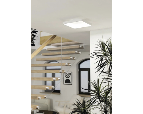 Vierkante LED-plafondlamp in een lichte, moderne woonruimte met een open houten trap en kamerplanten.