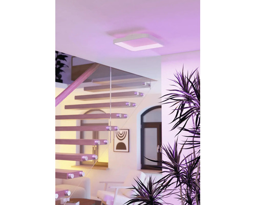 Vierkante LED-plafondlamp in een lichte, modern ingerichte woonkamer met houten trap en glazen leuning.