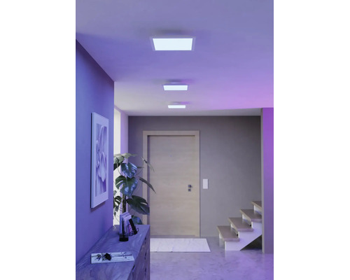 Drie vierkante LED-plafondpanelen in een moderne gang met een houten deur, trap en kamerplant.