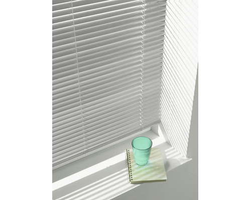 Jaloezie met horizontale lamellen voor een raam, die schaduwen werpt op een vensterbank met een glas en een notitieblok.