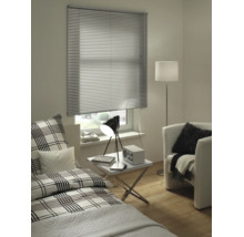 Moderne kamer met zilveren aluminium jaloezie voor het raam, bed met ruitjespatroon, witte bijzettafel en fauteuil.