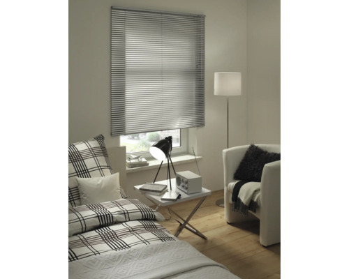 Moderne kamer met zilveren aluminium jaloezie voor het raam, bed met ruitjespatroon, witte bijzettafel en fauteuil.