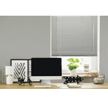 Een horizontale jaloezie voor een raam boven een modern ingericht bureau met monitor, lamp en decoratie in een werkkamer.