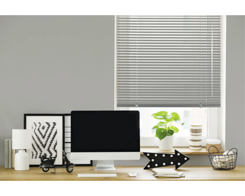 Een horizontale jaloezie voor een raam boven een modern ingericht bureau met monitor, lamp en decoratie in een werkkamer.