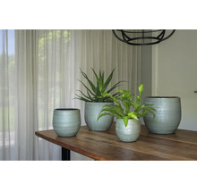 Vier gestructureerde plantenpotten in verschillende maten op een houten tafel in een lichte kamer, versierd met kamerplanten.