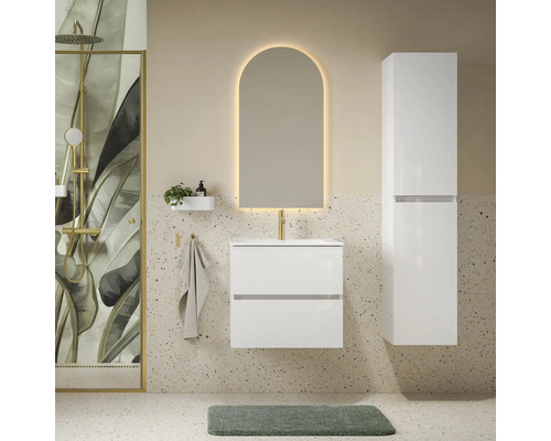 Moderne badkamer met wit wastafelmeubel, hoge zijkast, boogvormige spiegel met verlichting en douche met botanisch bladmotief.