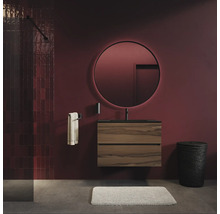 Moderne badkamer met ronde, verlichte spiegel boven een wandhangend wastafelmeubel met houtlook en zwarte kraan tegen donkere muren.