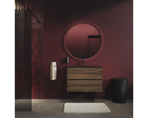 Moderne badkamer met ronde, verlichte spiegel boven een wandhangend wastafelmeubel met houtlook en zwarte kraan tegen donkere muren.