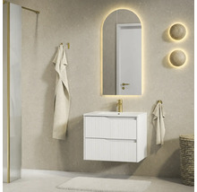 Moderne badkamer met wit badmeubel met ribbelstructuur, gouden kraan en boogvormige LED-spiegel op een beige tegelwand.