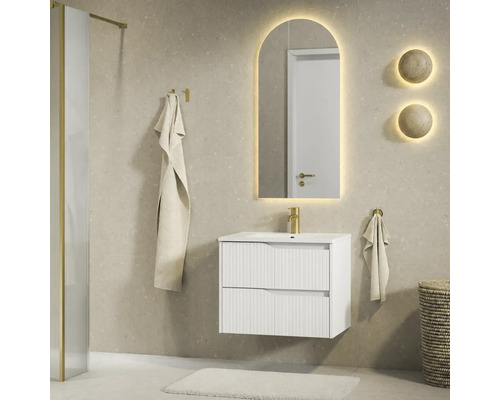 Moderne badkamer met wit badmeubel met ribbelstructuur, gouden kraan en boogvormige LED-spiegel op een beige tegelwand.