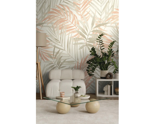Moderne woonkamer met palmbladbehang, witte bouclé fauteuil, glazen salontafel en groene kamerplant.