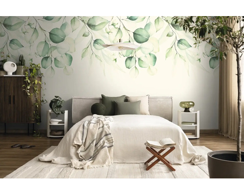 Lichte slaapkamer met een grote fotobehang van groene botanische bladeren, een bed met licht beddengoed en een donkerhouten kast.