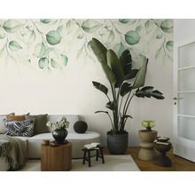 Fotobehang met aquarel bladerenmotief in een lichte woonkamer met een bank en een grote kamerplant.
