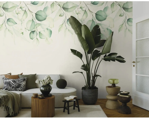 Fotobehang met aquarel bladerenmotief in een lichte woonkamer met een bank en een grote kamerplant.