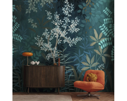 Vliesbehang met botanisch bladerpatroon in donkergroen en blauw, gecombineerd met een donker dressoir en een oranje fauteuil.