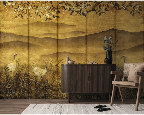 Fotobehang met Japans landschapsmotief met heuvels, kraanvogels en bloeiende takken in goudtinten achter een dressoir en stoel.