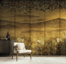 Fotobehang in Japanse stijl met kraanvogels, bergen en kersenbloesems in goudtinten in een woonkamer met fauteuil en dressoir.
