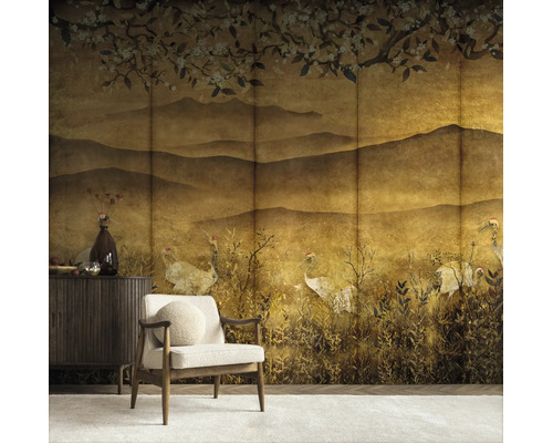 Fotobehang in Japanse stijl met kraanvogels, bergen en kersenbloesems in goudtinten in een woonkamer met fauteuil en dressoir.