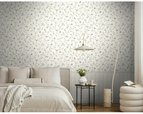Licht vliesbehang met blauw bloemenpatroon in een moderne slaapkamer met een licht bed, booglamp en bijzettafel.
