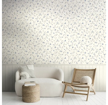Lichte woonkamer met bloemenbehang, witte bank, rotan stoel en houten wandpanelen.