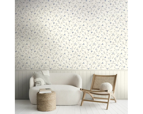 Lichte woonkamer met bloemenbehang, witte bank, rotan stoel en houten wandpanelen.