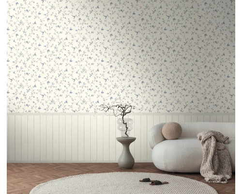 Bloemenbehang met kleine bloemen boven een witte lambrisering in een lichte kamer met een bank en visgraatvloer.