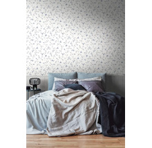 Lichte slaapkamer met bloemenbehang met fijne ranken en kleine bloemen. Het bed is opgemaakt met diverse kussens en dekens.
